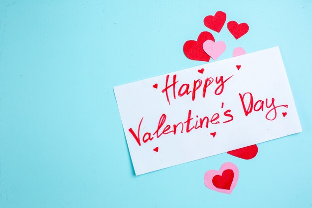 Photo top view happy valentines day written on paper red and pink hearts on blue background copy place