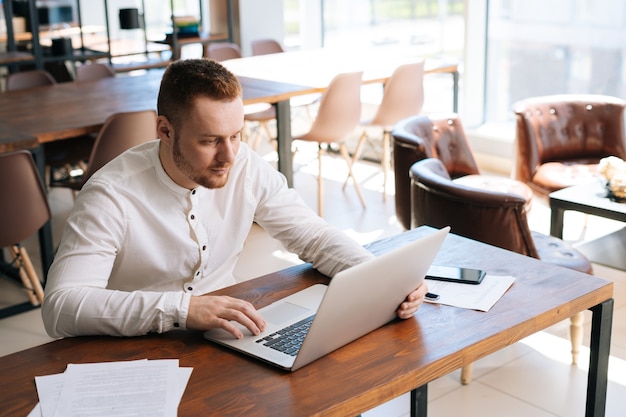 Top view of happy young man is working on laptop computer at the table in modern office room