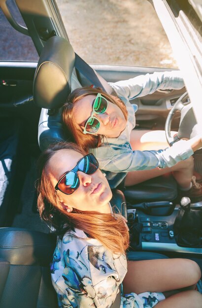 Top view of happy young women friends with sunglasses having fun inside of cabriolet car in a road trip adventure. Female friendship and leisure time concept.