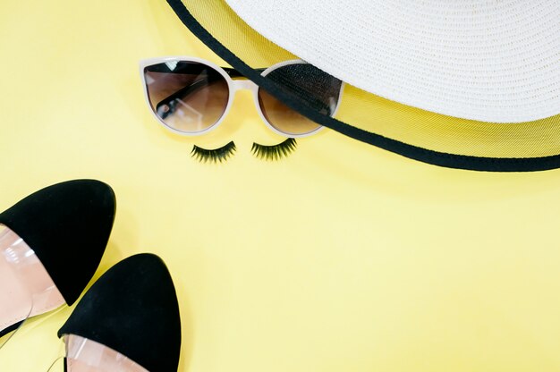 Top view hat and sunglasses on yellow background with sunlight and shadow of coconut leaves.