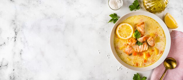 Top view of a healthy creamy salmon soup in a plate on white surface. Diet food. Copy space. Long banner