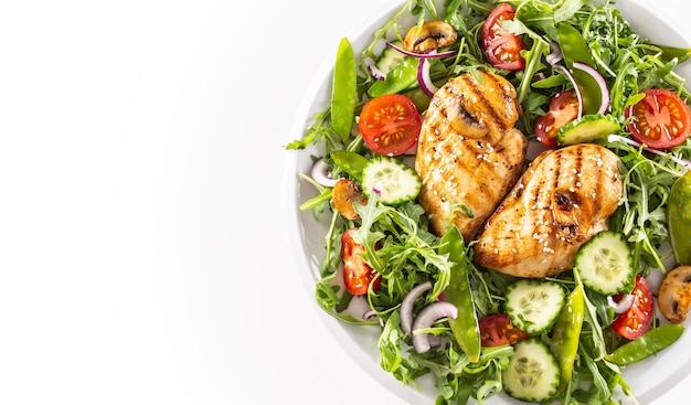 Photo top view healthy salad with grilled chicken topped with sesame seeds, rocket, spring peas, cherry tomatoes, sliced cucumber, grilled mushrooms and red onion, isolated on right half of the white backgr