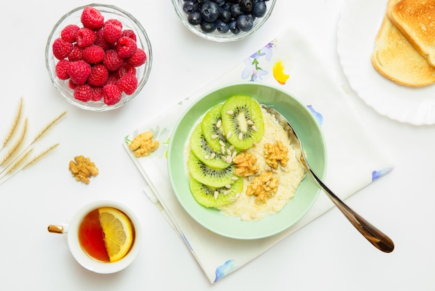 Foto vista dall'alto di una sana colazione gustosa, porridge con frutta, noci, frutti di bosco, pane tostato e una tazza di tè al limone