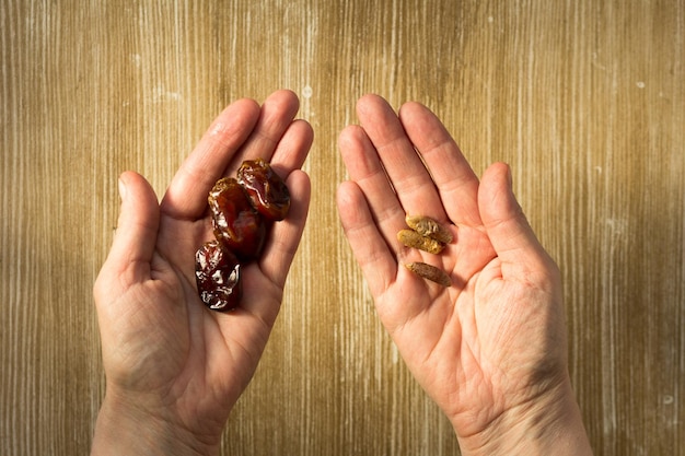 Top view of heap of date fruit on one woman hand and bones as seeds on other hand for planting palm on the wooden background