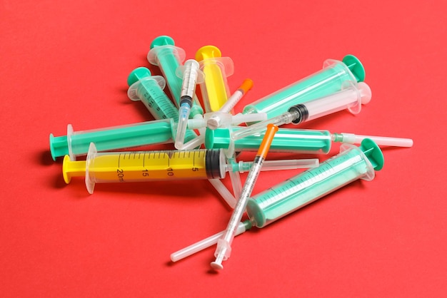 Top view of a heap of syringes and insulin syringes at red background Medical injection concept with copy space