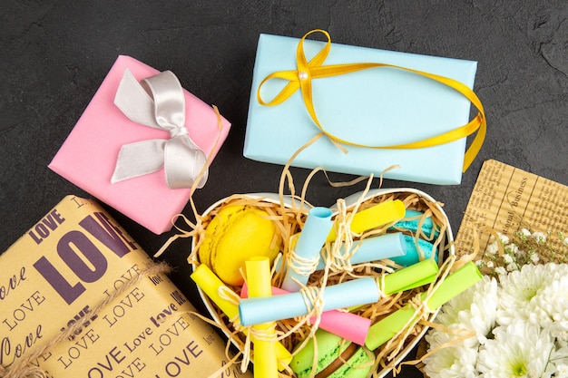 top view heart shaped box with rolled up sticky notes and macarons wrapped gifts flower bouquet on dark background