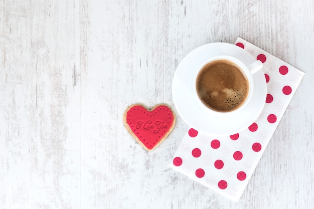 Top view of a heart shaped cookie and a cup of coffee.