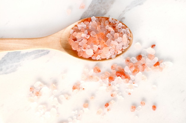 Top view of himalayan pink salt in wooden spoon on white marble table.