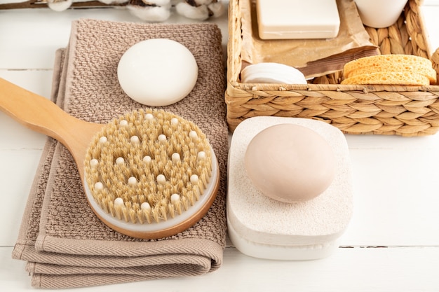 Top view of home spa accessories water hyacinth box with sponges, soap and natural oil, brush for dry massaging and cotton towel on wooden background.