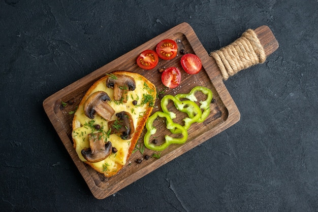 Top view of homemade tasty snack with mushrooms and chopped vegetables on wooden board on black background