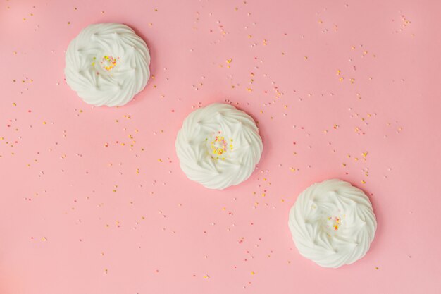 Top view of homemade white air meringues and confectionery decorations on pink