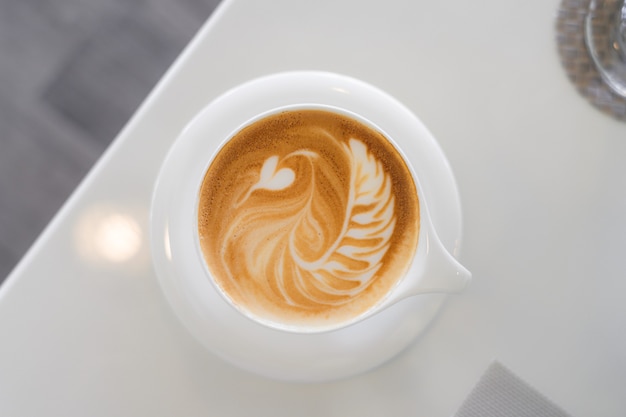 Top view of hot coffee with latte art in a white cup and saucer on white table in the cafe