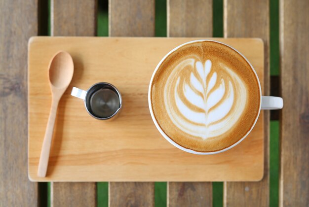 Top view hot latte coffee with hearts pattern and syrup on wooden table