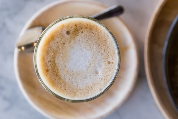 Photo top view of hot latte in a glass cup with spoon and wooden plate.