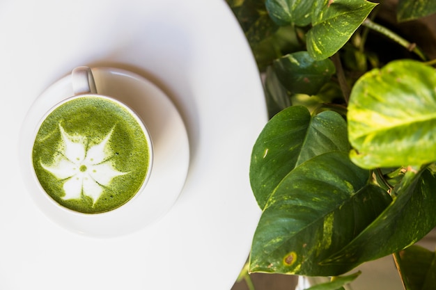 Vista superiore della schiuma di tè verde matcha caldo sul tavolo bianco con foglie verdi