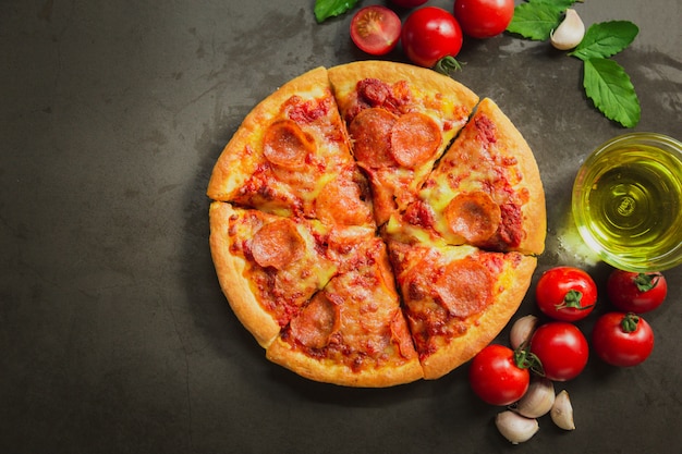 Top view of hot pepperoni pizza,Tasty pepperoni pizza and cooking ingredients tomatoes basil on black background.