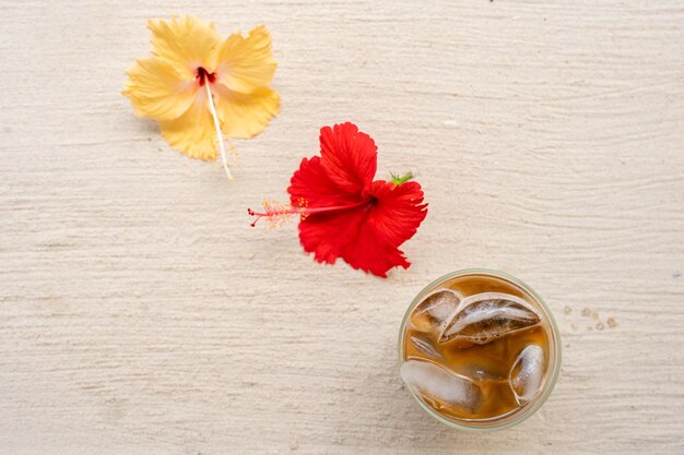 Top view iced coffee next to hibiscus flowers on the beach.