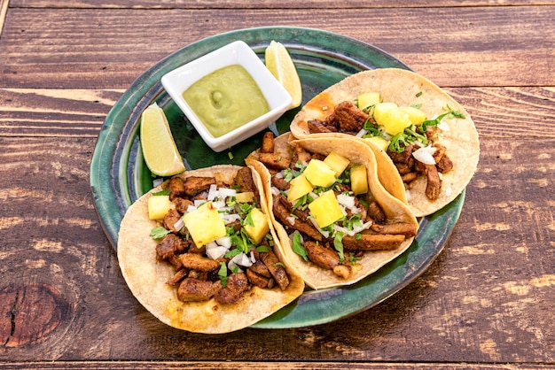 Top view image of delicious Mexican al pastor tacos with lime wedges corn tortillas and some guacamole on a beautiful green plate