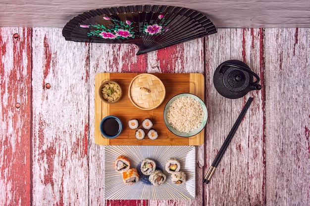 Foto immagine vista dall'alto di maki uramaki teiera nera bacchette nere california roll dim sum cesto vapore salsa di soia ventaglio nero e tavolo rosso e bianco