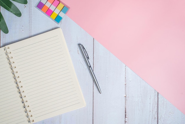 Top view image of notebook with pen and xanadu leaf on wooden table with pink background