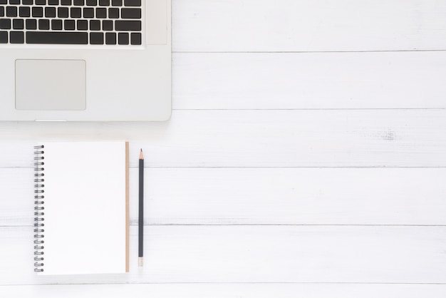 Top view image of open notebook with blank pages and laptop on wooden table