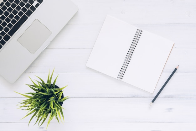 Top view image of open notebook with blank pages and laptop on wooden table