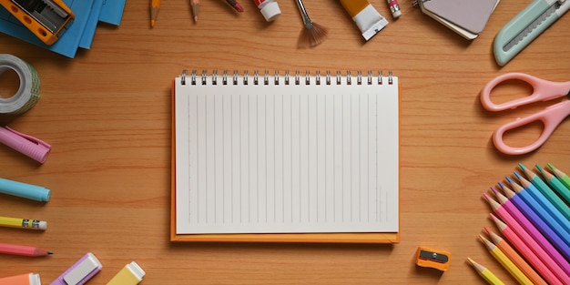 Top view image of the student desk is surrounding by an empty notebook and stationary.