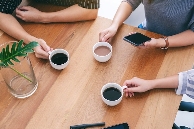 Top view image of three people holding coffee cups to drink on wooden table