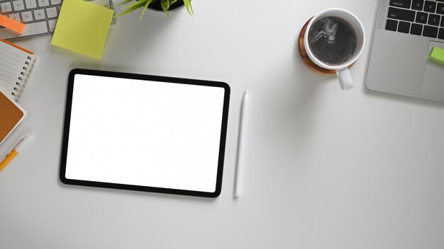 The top view image of white workspace is surrounding by a white blank screen tablet and various equipment.