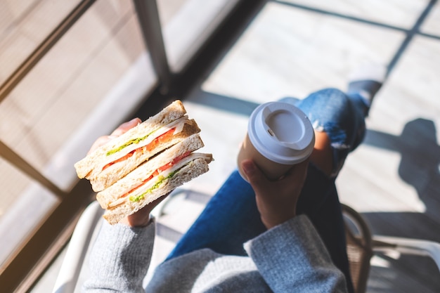 朝に全粒粉サンドイッチとコーヒーを持って食べている女性の上面画像