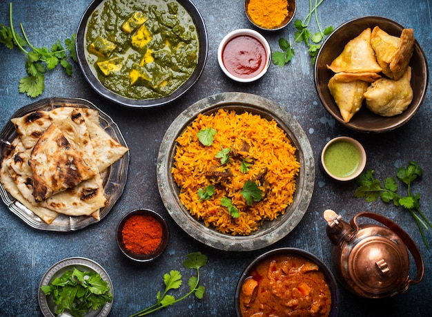 Top view of Indian traditional dishes and appetizers: chicken curry, pilaf, naan bread, samosas, paneer, chutney on rustic background. Table with choice of food of Indian cuisine, dinner/buffet