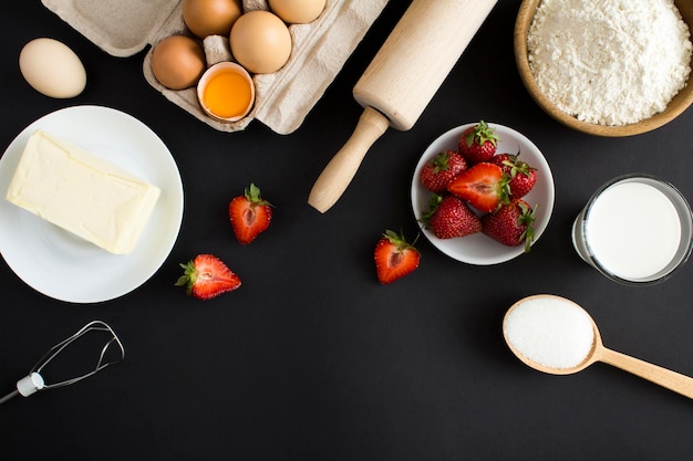 Vista dall'alto degli ingredienti per preparare una torta di fragole o una torta sullo sfondo nero spazio di copia