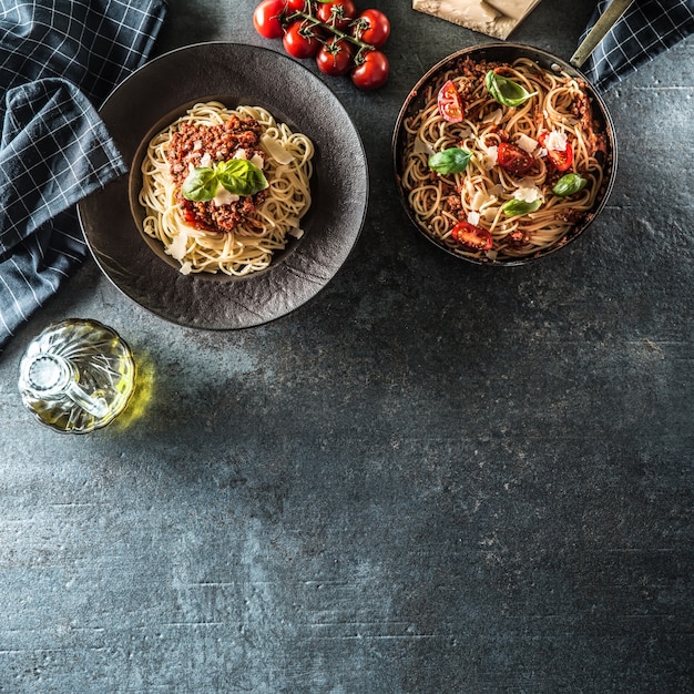 Top of view italian pasta spaghetti bolognese in plate and pan with tomatoes and basil.