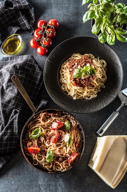 Spaghetti alla bolognese di pasta italiana vista dall'alto in piatto e padella con pomodori e basilico.