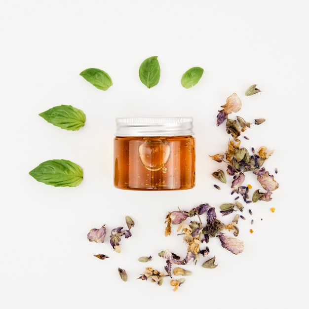 Top view jar of honey with leaves and flowers around