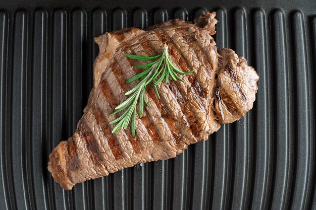 Top view of juicy roasted steak made of grainfed beef meat laying on grill decorated with rosemary