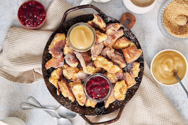 Top view of kaiserschmarrn with torn pancakes, cranberries jam, and apple puree on a table