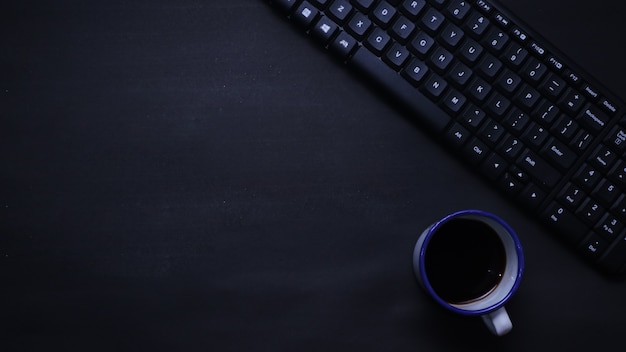 Vista dall'alto della tastiera e del caffè su sfondo piatto nero