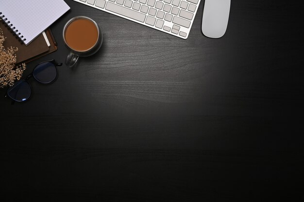 Photo top view keyboard, glasses, glasses and notebook on dark background.