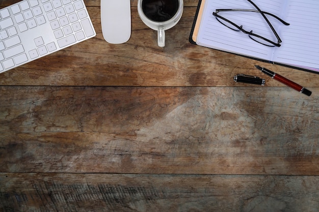 Photo top view keyboard, notebook, glasses and coffee cup on wooden table.