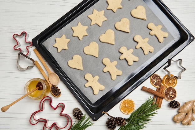 Top view of laid out gingerbread cookies on pastry rack. Cookies cutter, honey, pine scones and branches, dried slices of orange on wooden surface. Cooking process. Christmas preparations. 25 December