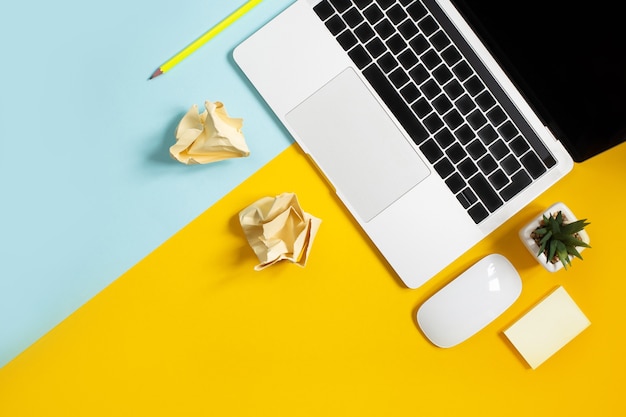 Top view of laptop, cactus, computer mouse, pencil on yellow and blue