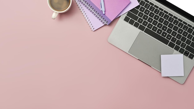ピンクの背景にラップトップ コンピューターの付箋ノートとコーヒー カップの上から見る