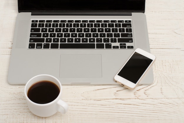 Top view of a laptop keyboard, smart phone and a cup of coffee