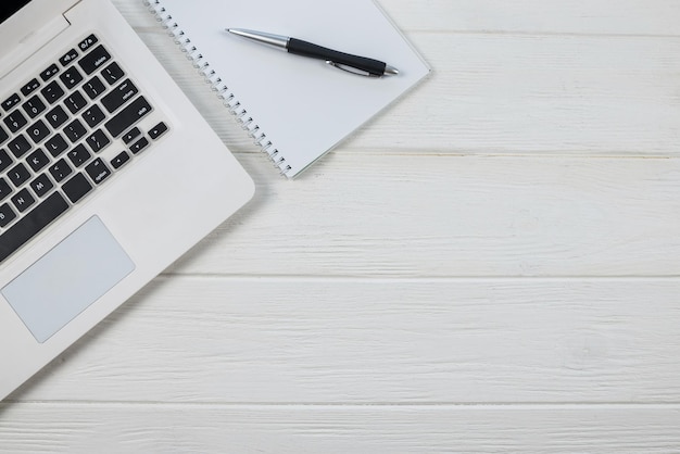 Top view of laptop keyboard with white blank notepad and pen on white background copy space place for text