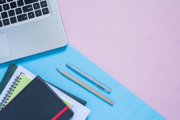 Top view of laptop, notebook, pen, pencil on blue and pink pastel color bakcground