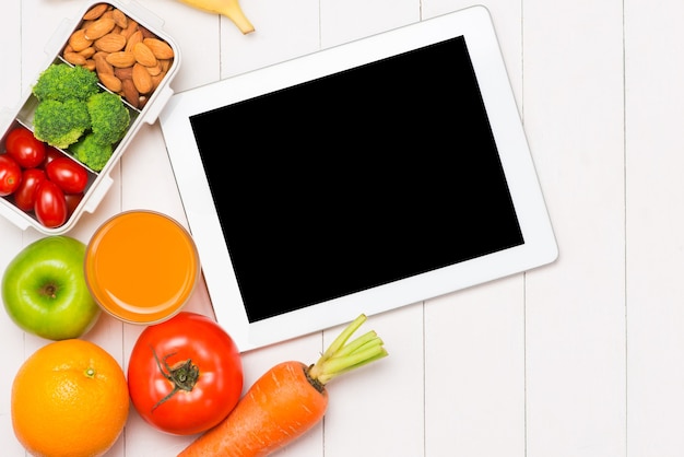 Top view of laptop, orange juice in glass and fresh salad in lunch box with plastic utensils at workplace