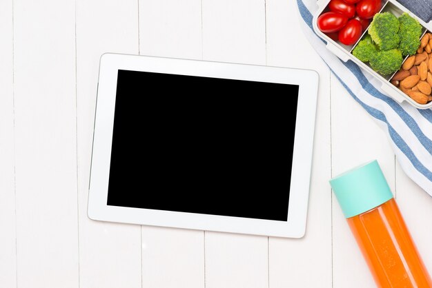 Top view of laptop, orange juice in glass and fresh salad in lunch box with plastic utensils at workplace