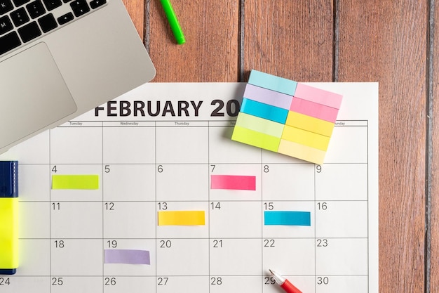 Top view of laptop with calendar of the month and several\
colored adhesive notes to highlight