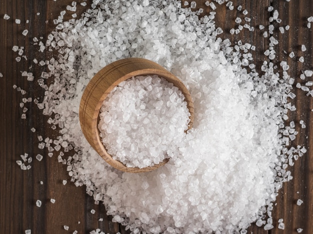 Top view of a large amount of scattered salt with a wooden Cup. Ground stone sea salt.
